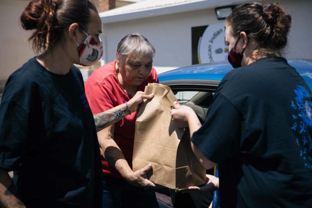 Volunteers helping woman load a bag into her car
