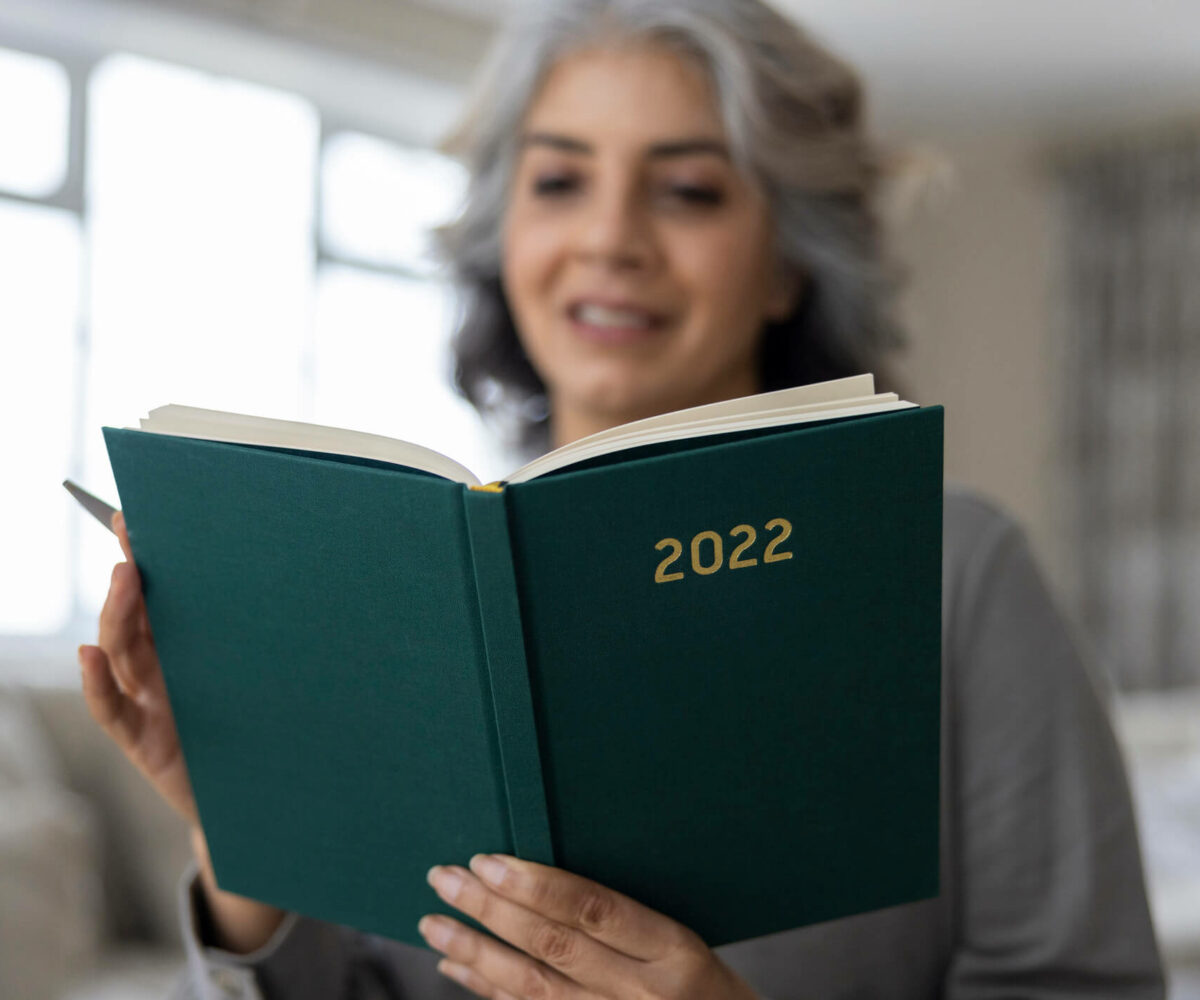 Older woman writing her goals in 2022 planner.