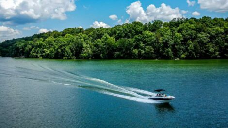 boat swiftly moving across a lake on a partially cloudy sunny day with full green trees on the shore.