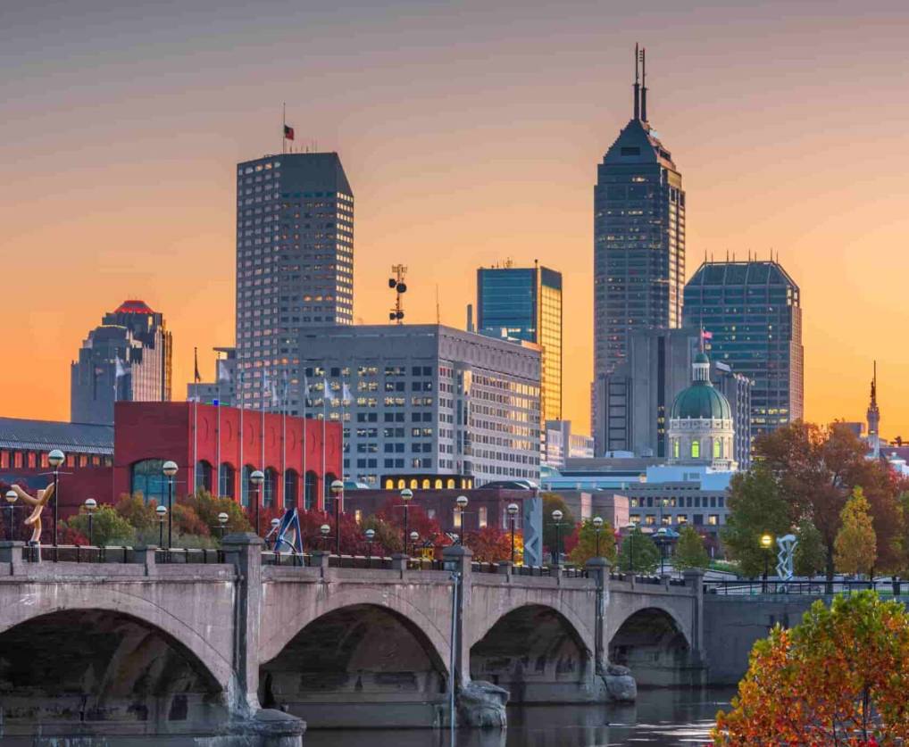 skyscrapers and other buildings in downtown Indianapolis with their lights on during a sunset