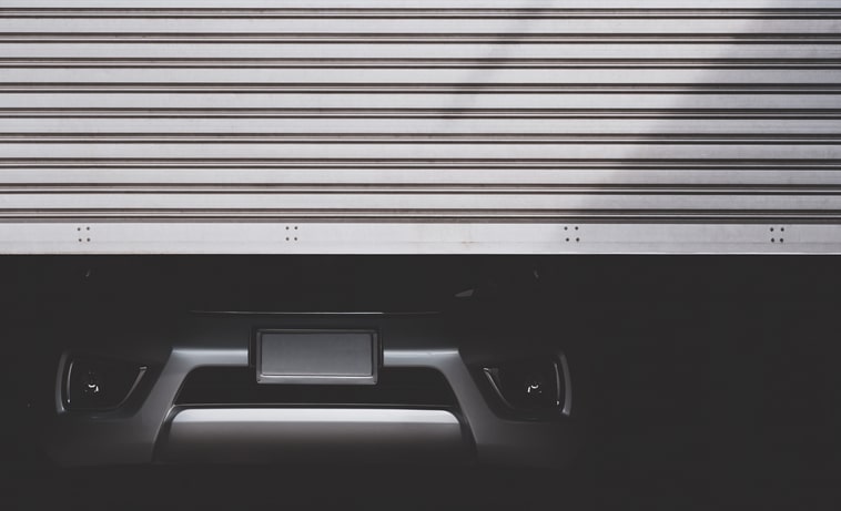 The bottom half of a silver car is seen as a garage door opens in front of it