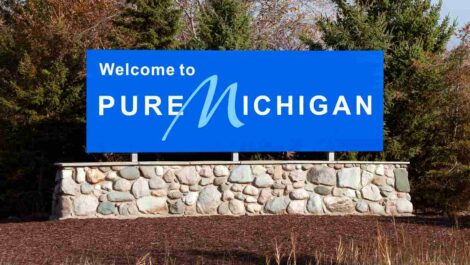 A bright blue sign outdoors reads Welcome to Pure Michigan