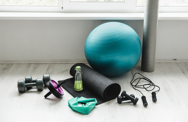 A pile of workout equipment including weights, a sweatband, workout mat, exercise ball, and jump rope