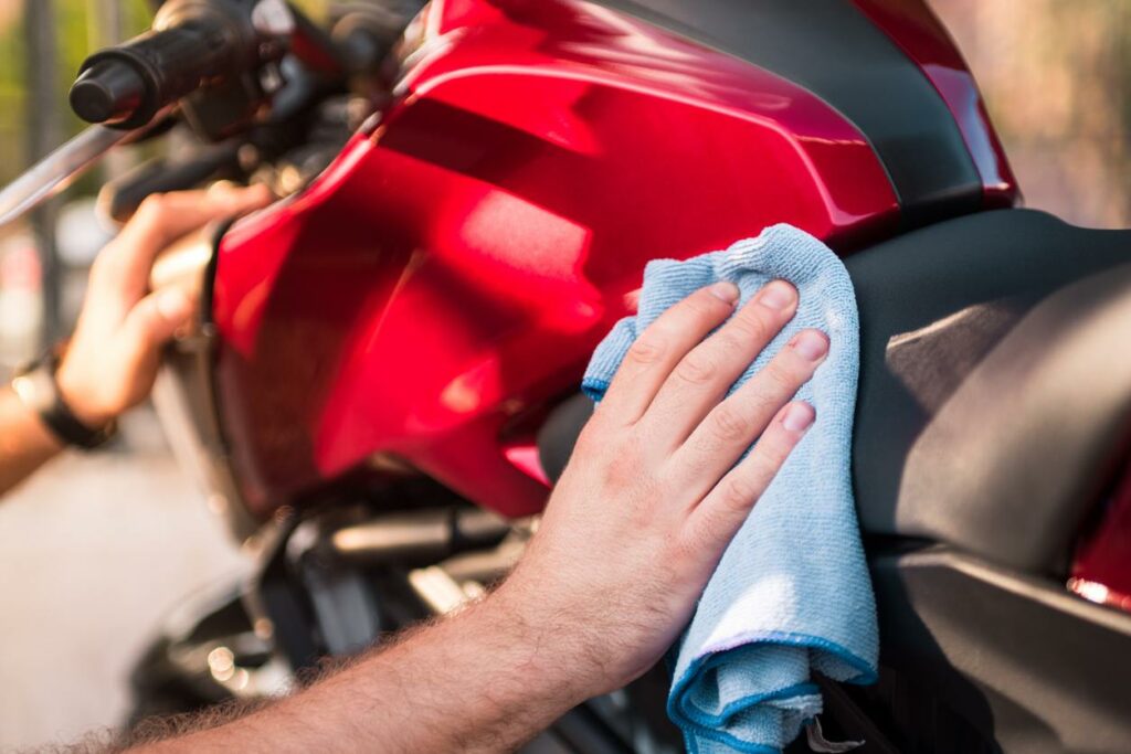 A man uses a blue microfiber cloth to wipe the seat of a red and black motorcycle