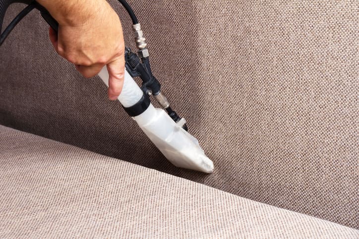 Person hand-vacuuming a couch.