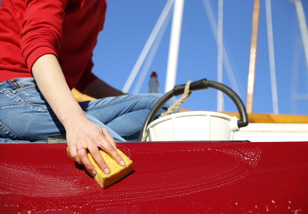 A person cleaning the outer surface of a boat with a sponge.