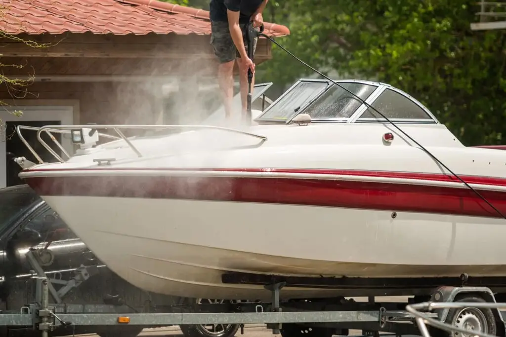 Man standing on and power washing a boat.
