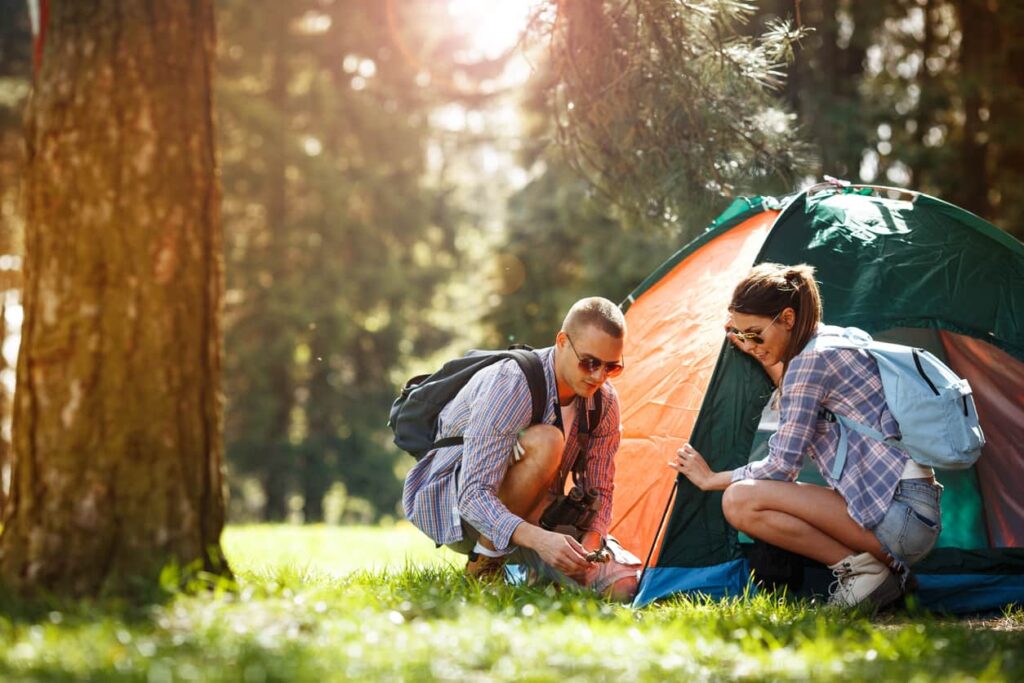 Couple pitching a camping tent in a grassy, wooded area.