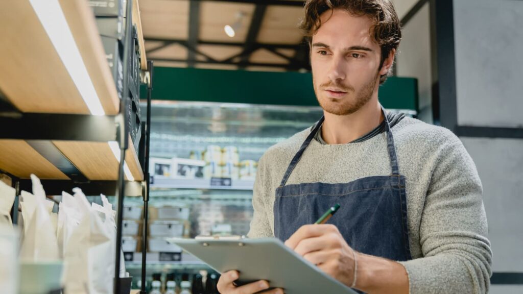 Person in apron with a clipboard takes inventory of sealed products.