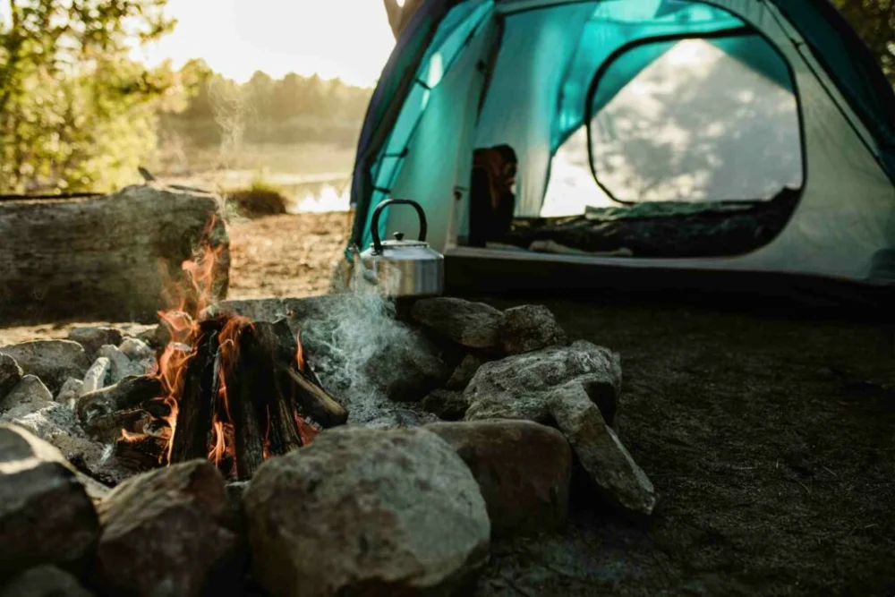 A tent and campfire near a pond.