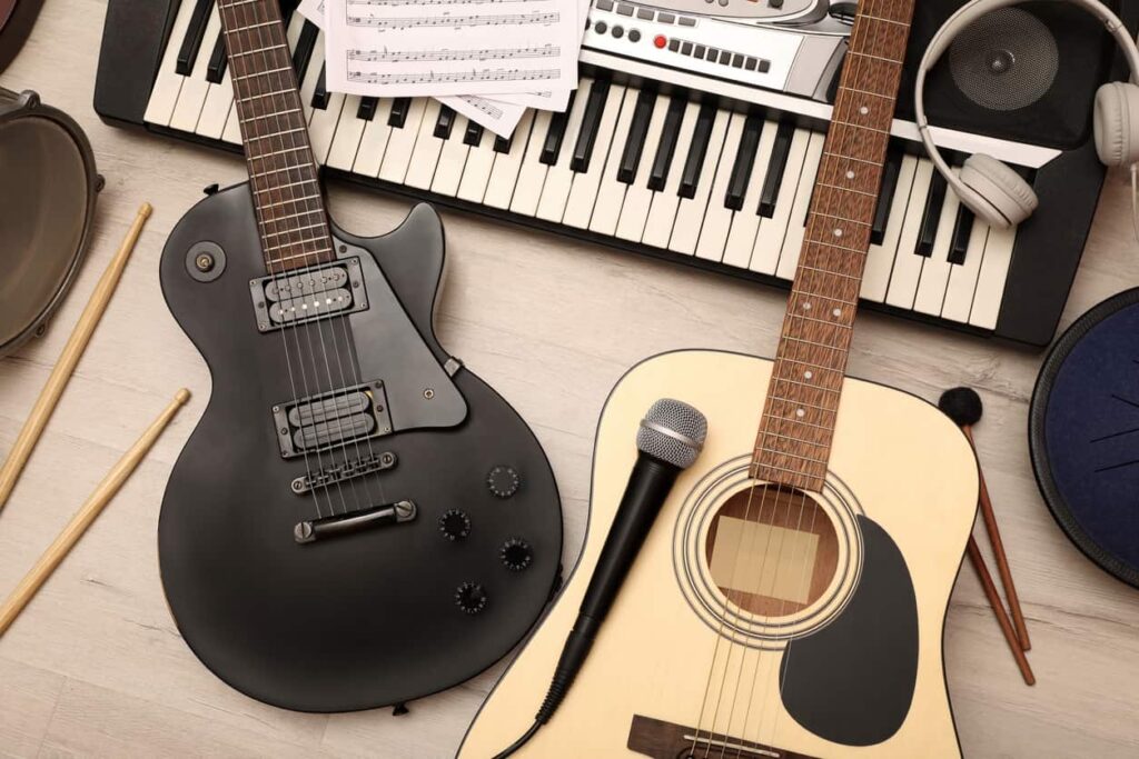 Electric guitar, acoustic guitar, piano, microphone, and sheet music sit on a wooden floor.