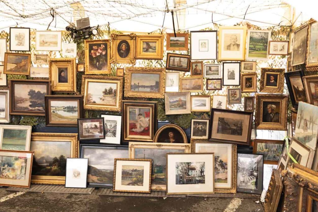 Assorted, framed paintings hang in a display.