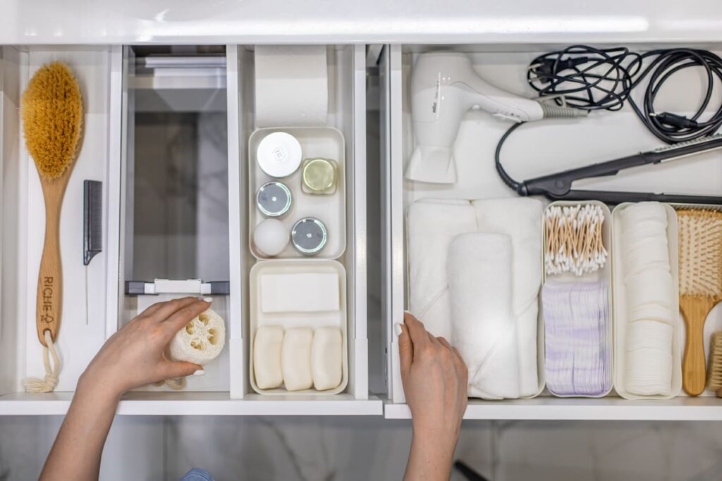 Top view of woman’s hands neatly organizing bathroom amenities and toiletries in drawer or cupboard in the bathroom.