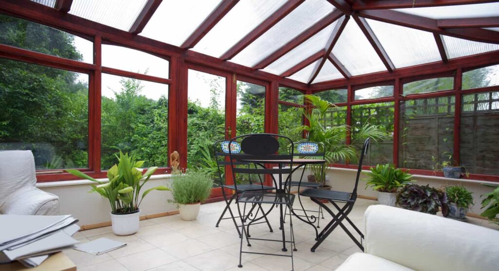 Chairs around a table in a furnished and plant-filled sunroom space.