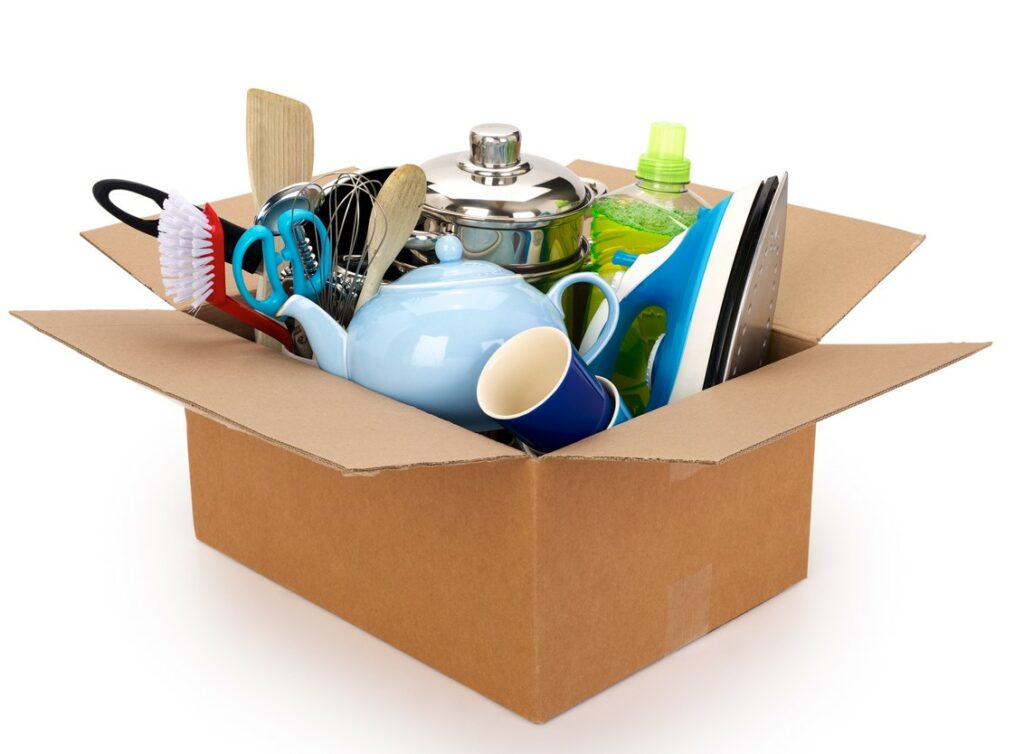 Pots, pans, dishes, utensils, and other household items in a cardboard box.