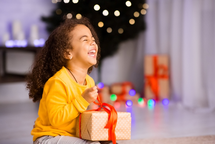 A little girl laughs as she unwraps a present on Christmas.