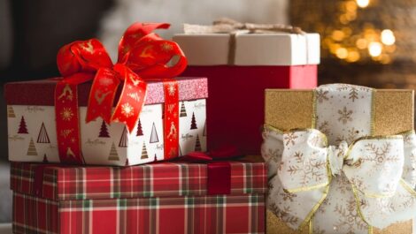 A pile of wrapped Christmas presents before a lit Christmas tree.