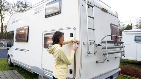 A woman in a yellow hoodie locks the back door of a white RV parked outdoors.